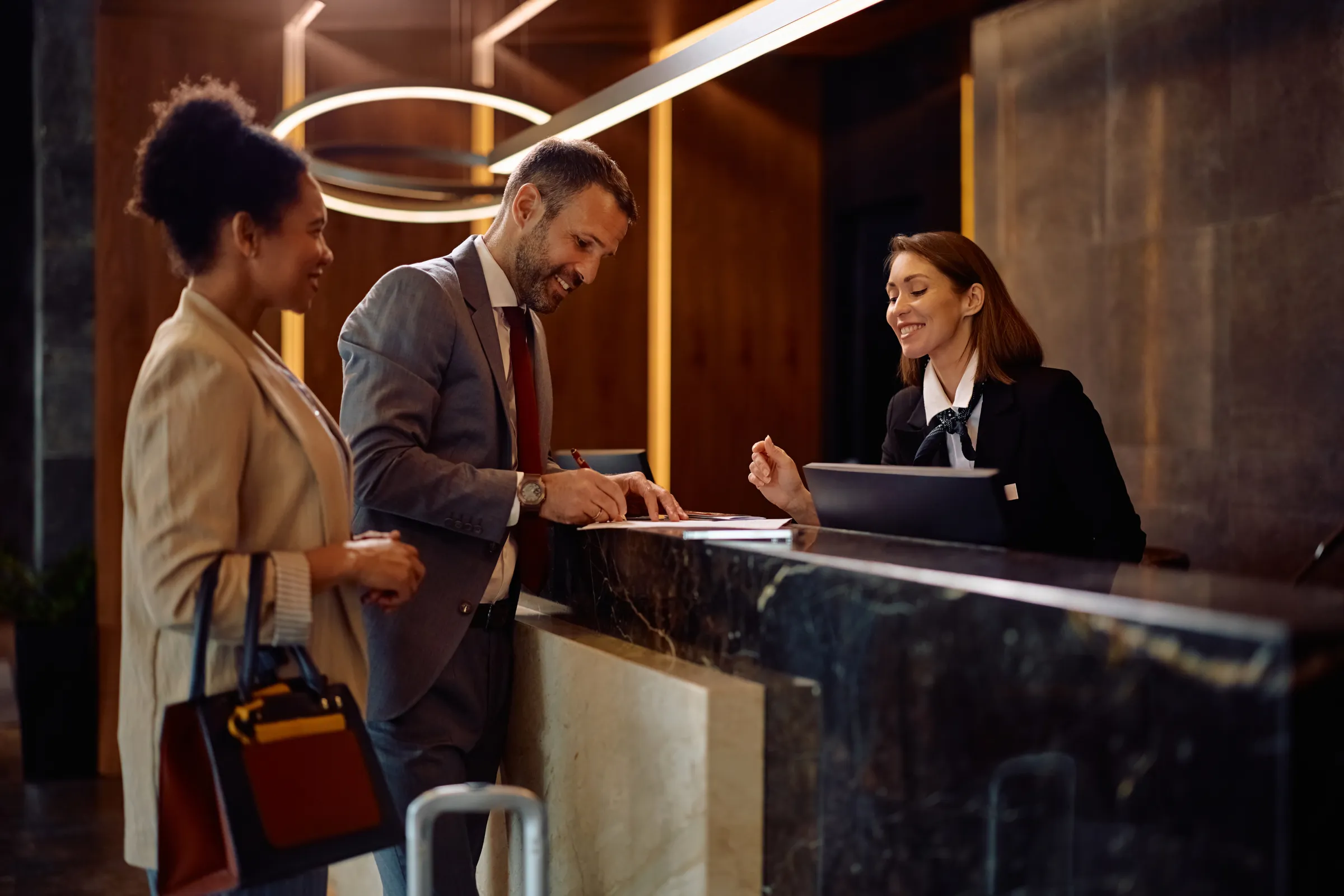 Hotel concierge assisting two guests at a softly lit front desk